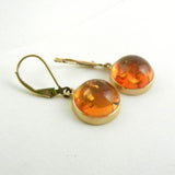 Custom design 14kt yellow gold earrings with round and polished cabochon amber is bezel set and hanging from leverback earrings.