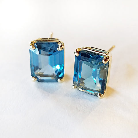 Emerald cut blue topaz shimmers like the Caribbean sea and is set in custom made gold stud earrings.